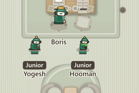 Two small robots, Yogesh and Hooman, sitting on the floor behind their lead, Boris, each with a laptop in front of it. Each name tag has two rows: a dark chip reading Junior, and the name under it.